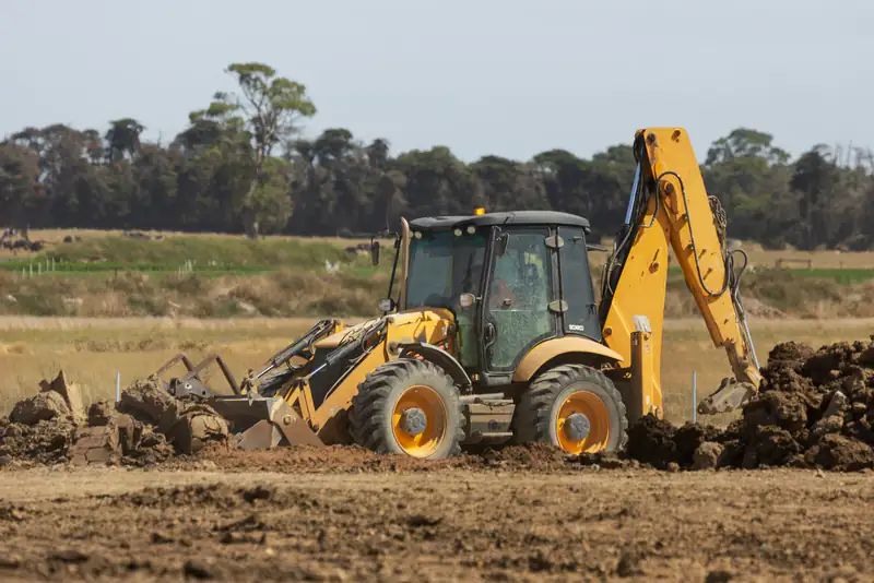 A yellow backhoe digging soil on a residential building site (stock photo)